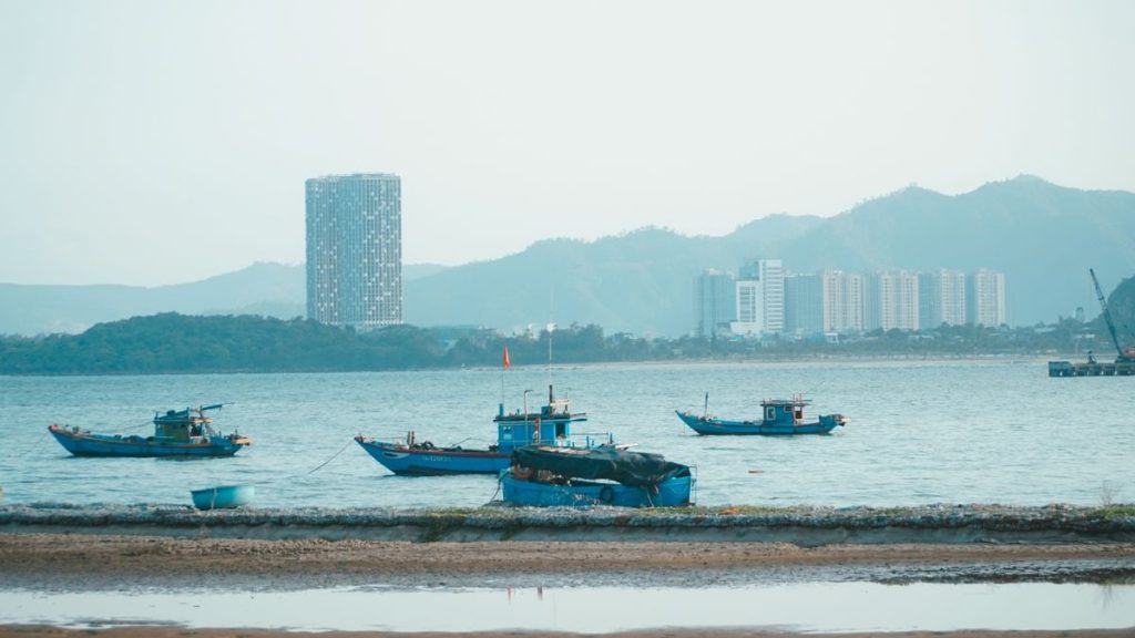 Scenic view of fishing boats in Da Nang harbor with urban skyline and mountains.